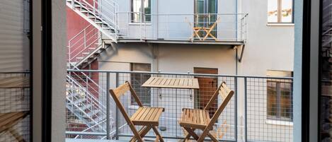Un balcone con due sedie di legno e un tavolo, una ringhiera in metallo e una scala antincendio a sinistra.