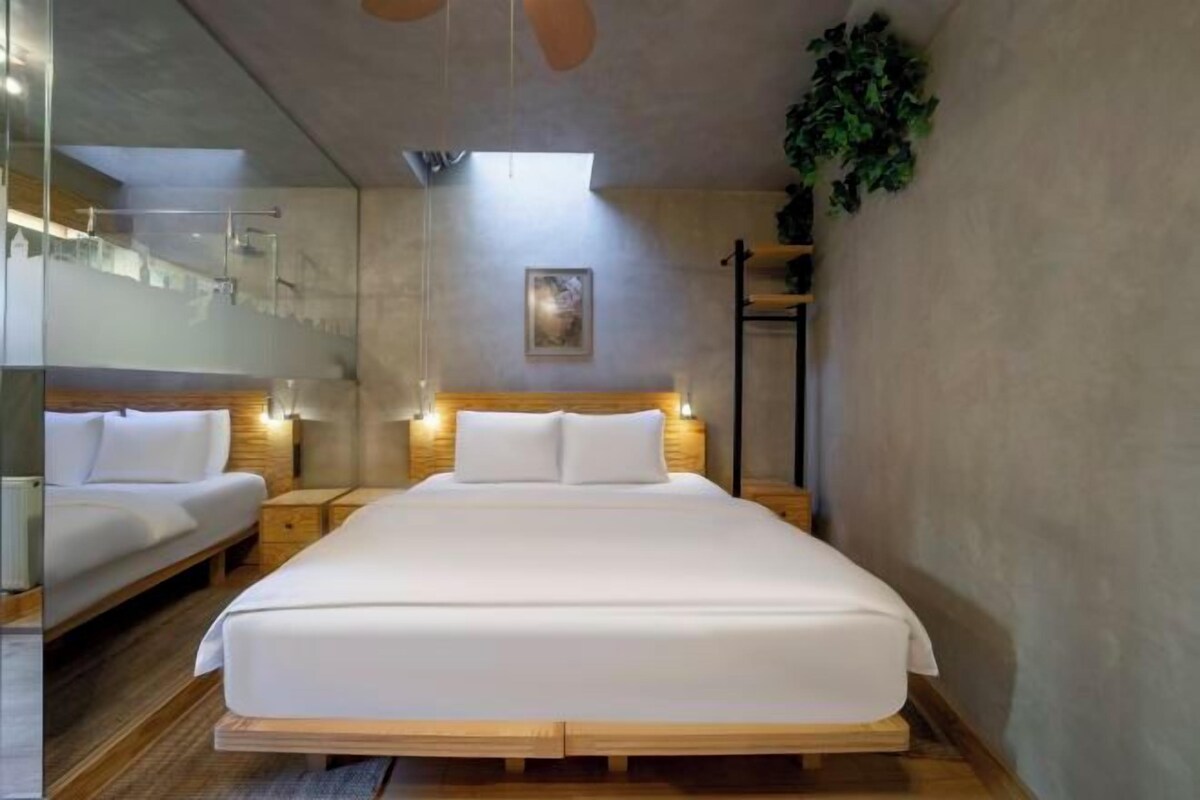 A modern bedroom with a large bed, bedside tables, a mirror, and a wall-mounted plant.
