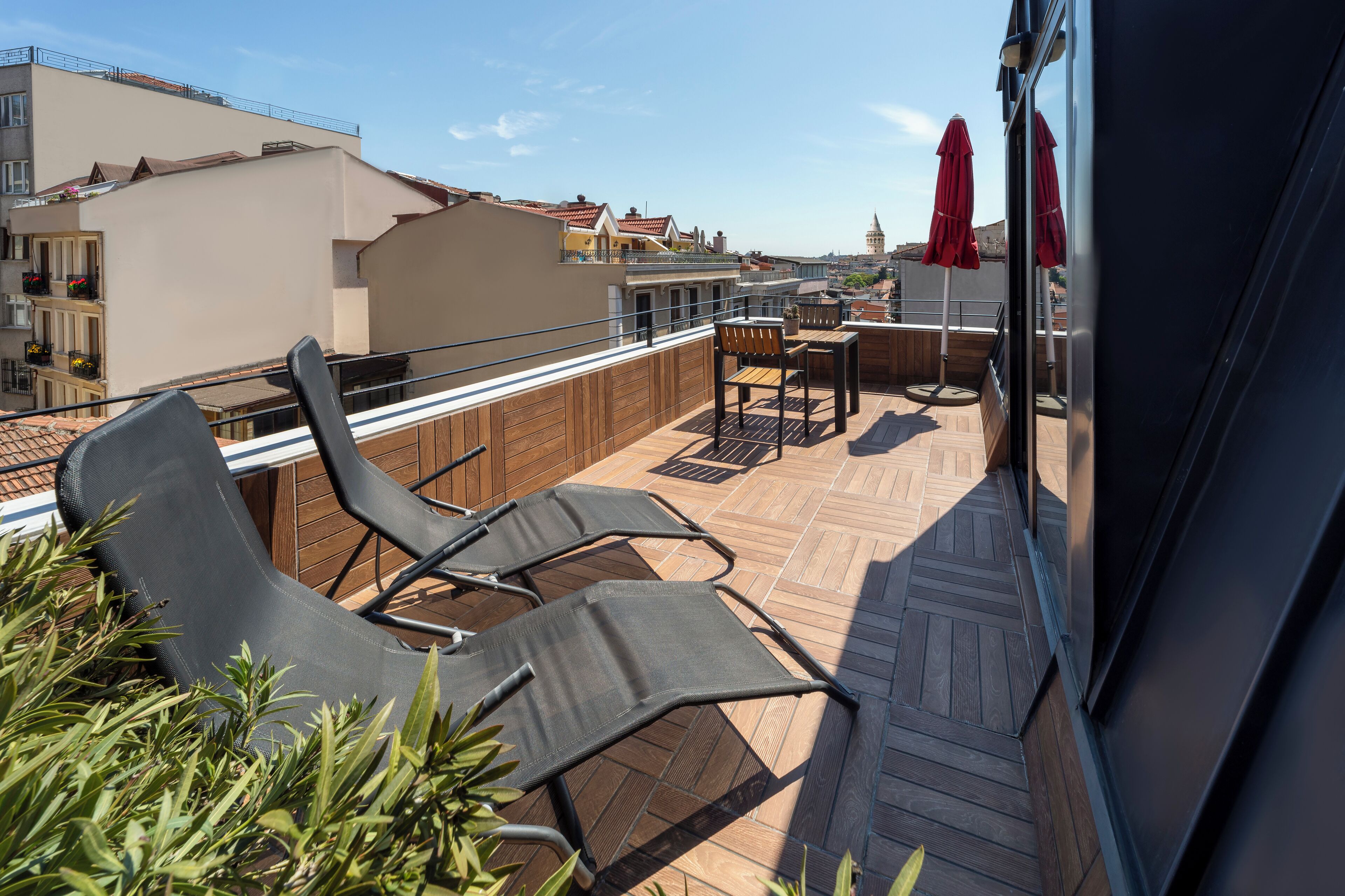 Eine Dachterrasse mit Liegestühlen, einem Tisch und roten Sonnenschirmen.