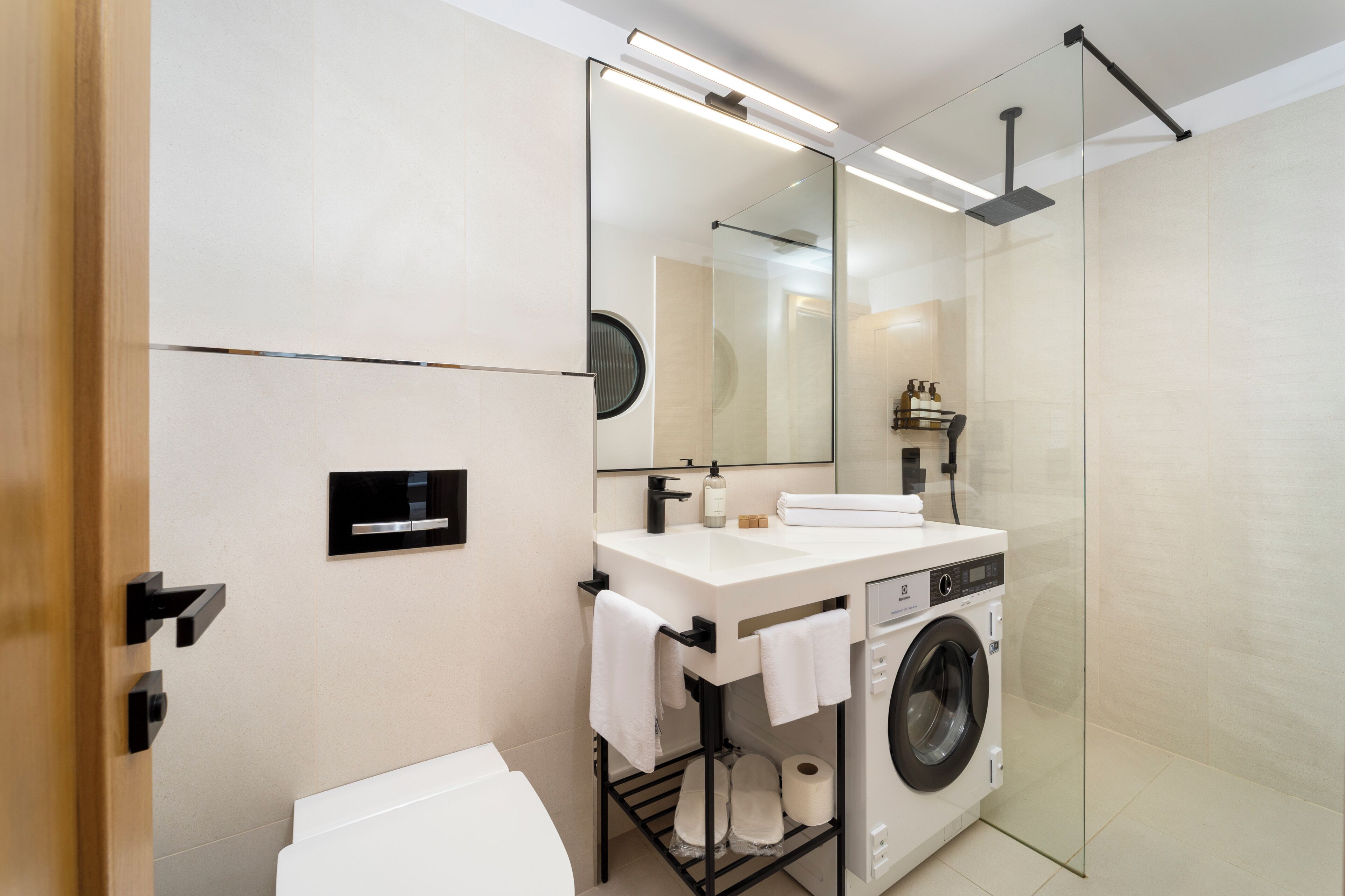 A modern bathroom with a glass shower enclosure, a built-in washing machine, and a large mirror above the sink.