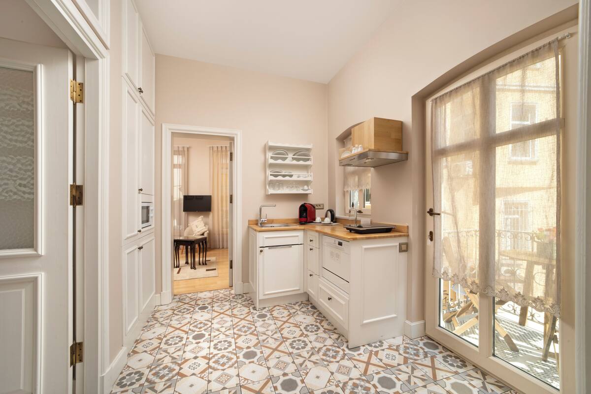 Une cuisine de taille réduite avec des meubles blancs, un plan de travail en bois et un sol carrelé à motifs.