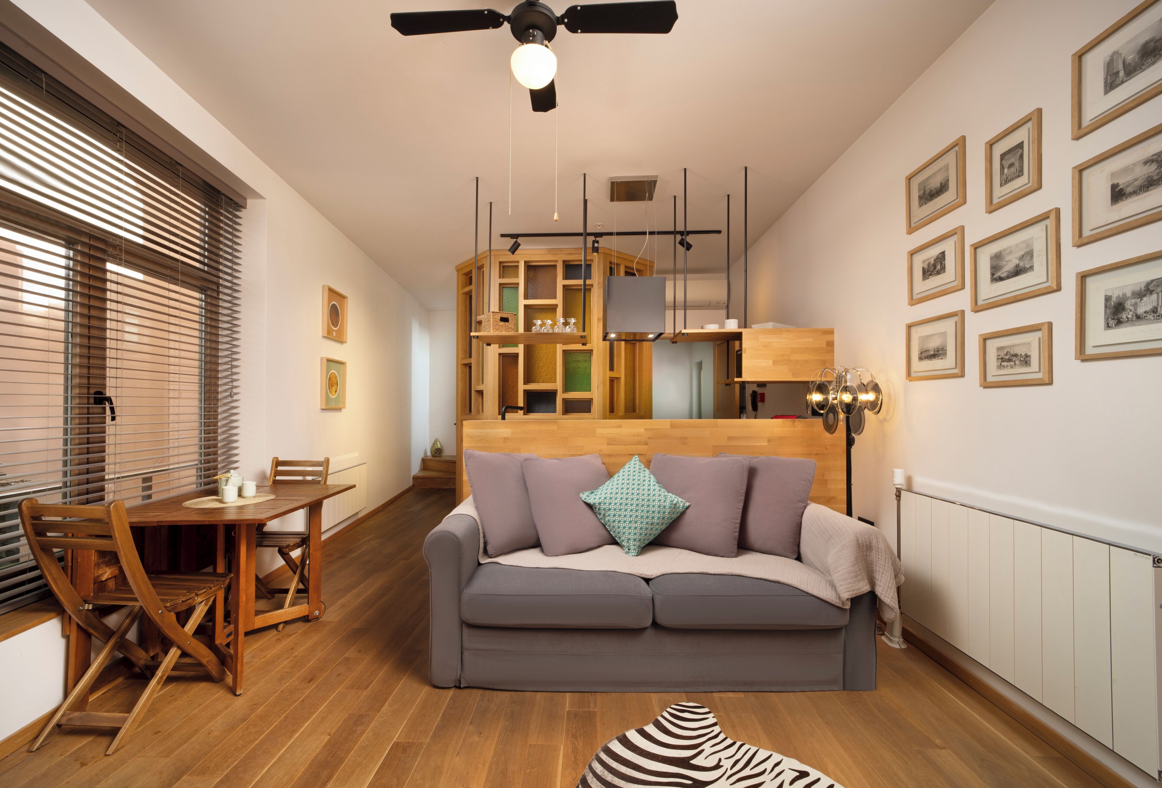 A modern living room with a sofa, dining table, and chairs. There is a ceiling fan, a fireplace, and framed pictures on the wall.