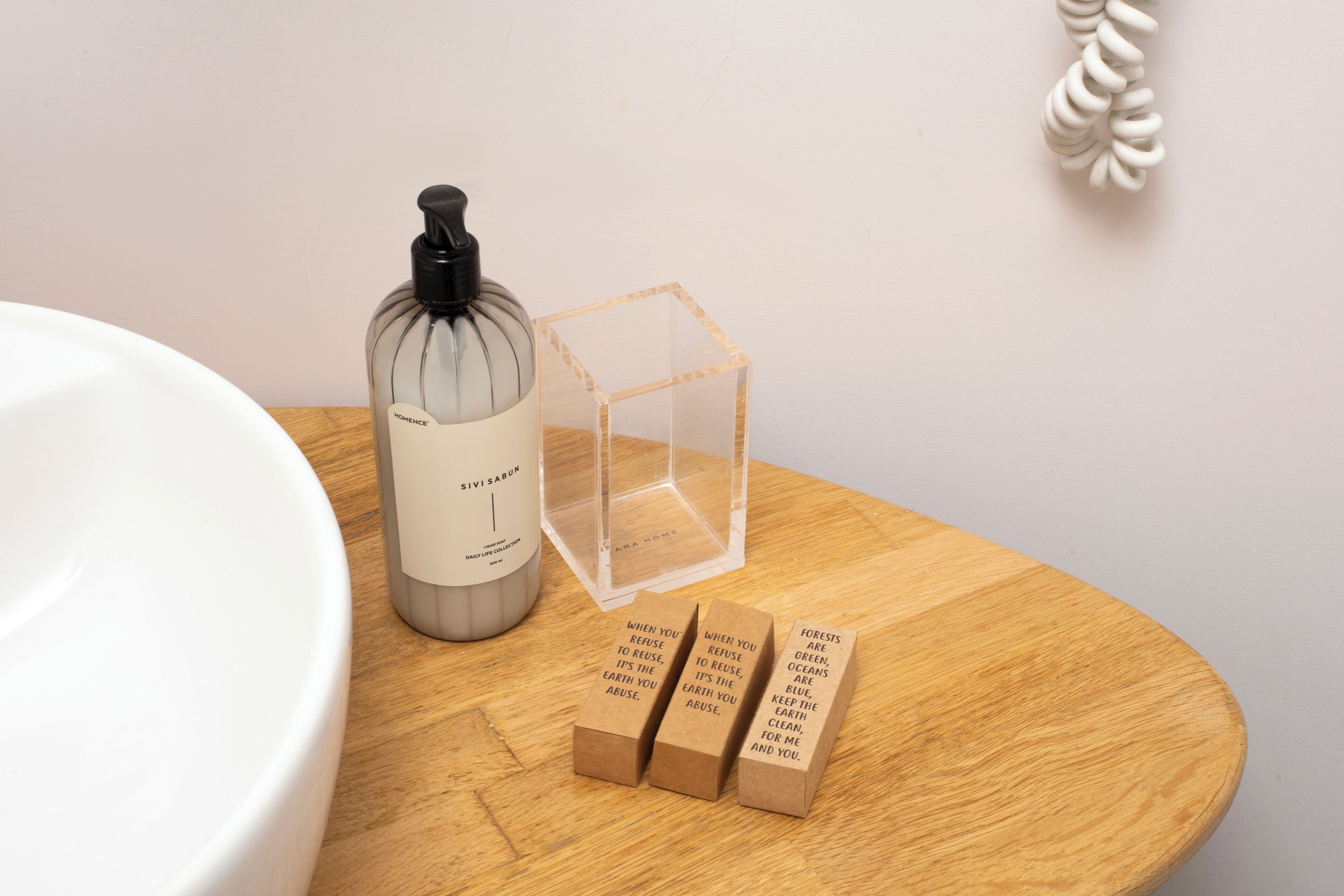 A bathroom with a white sink, a glass bottle, a clear cube, and three brown boxes with text.