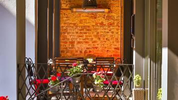An outdoor seating area with a brick wall backdrop, metal railings, and potted plants.