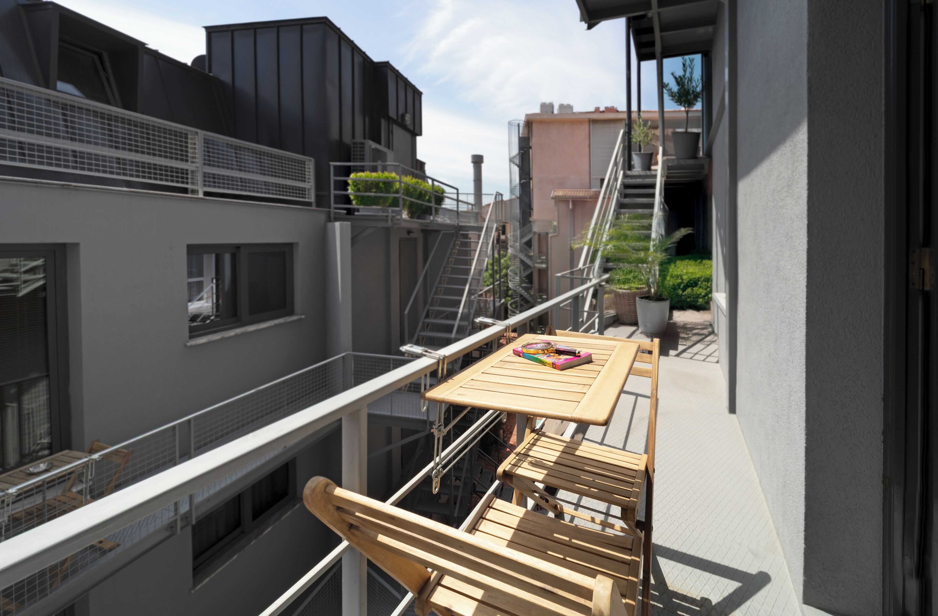 A balcony with a wooden table and chairs, a small potted plant, and a view of adjacent buildings.