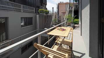 A balcony with a wooden table and chairs, a small potted plant, and a view of adjacent buildings.