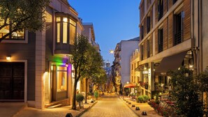 Une rue étroite pavée, bordée d’immeubles dotés de balcons et d’espaces aménagés pour s’asseoir à l’extérieur.