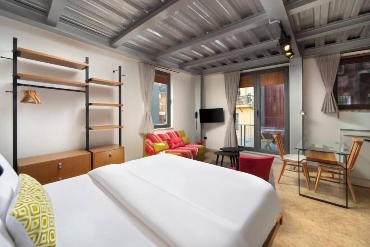 Une chambre d’hôtel avec un lit, un bureau, une chaise, une télévision et une fenêtre.