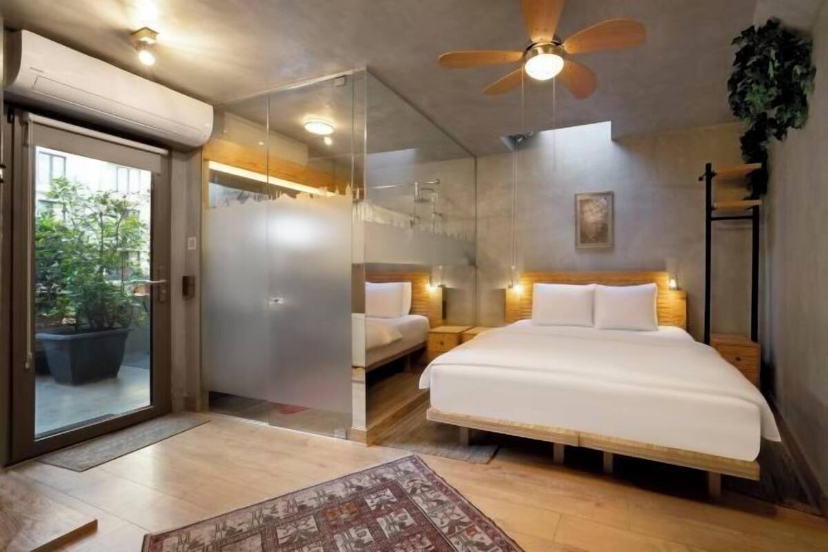 Une chambre moderne avec un grand lit, un ventilateur de plafond et une cloison en verre.