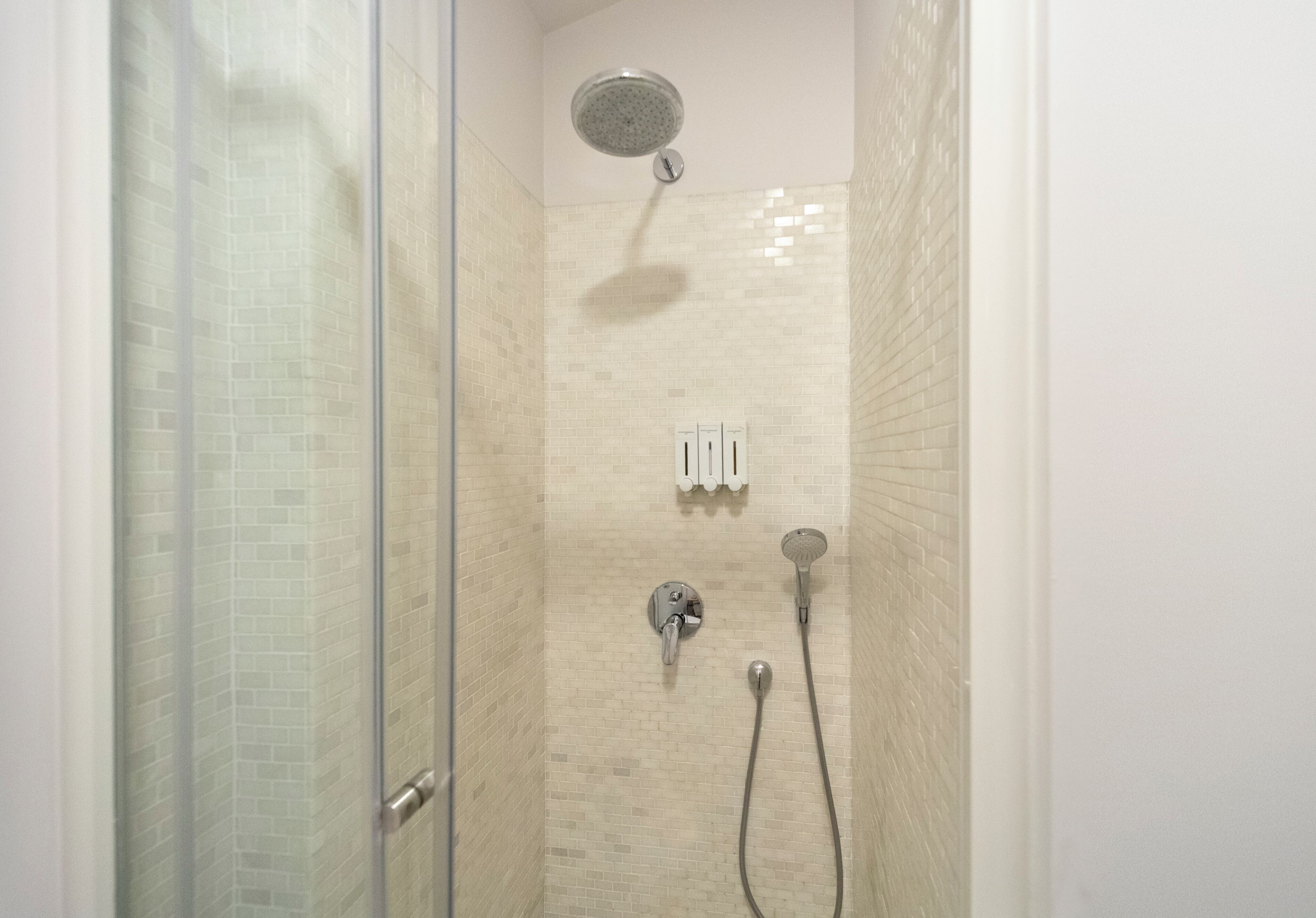 Ducha con puerta de cristal, cabezal de ducha manual y grifo empotrado en la pared.