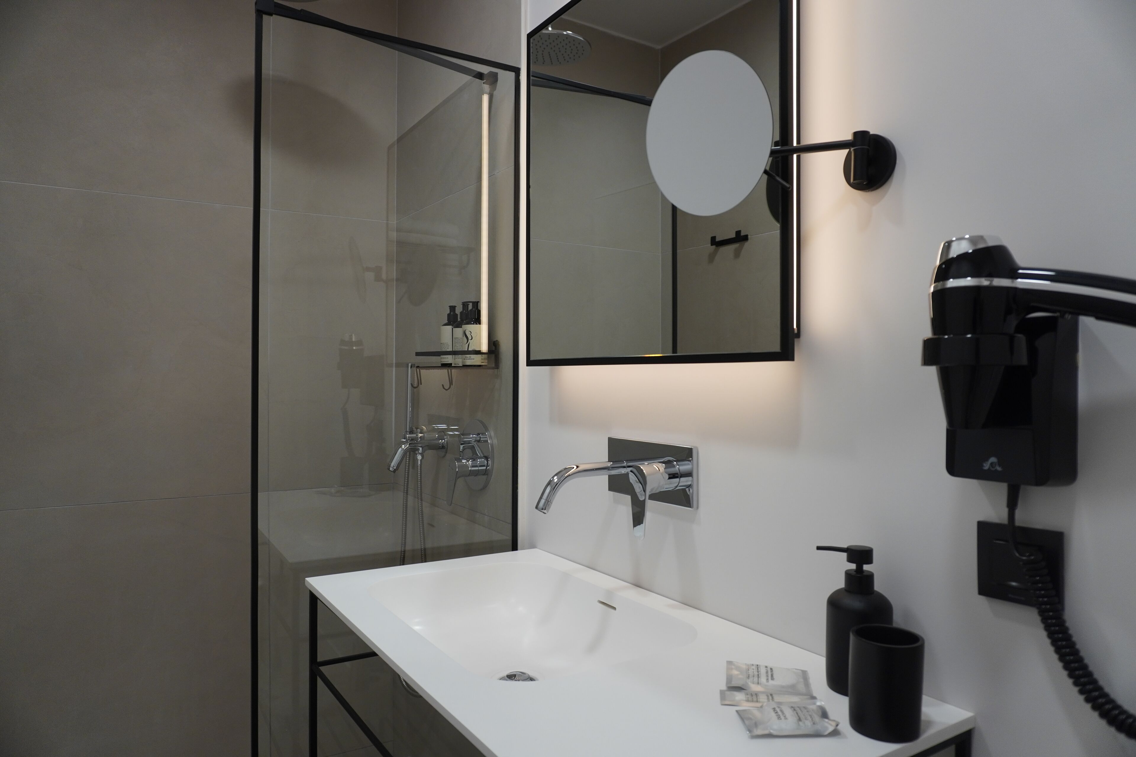 A modern bathroom with a glass shower enclosure, a white sink, and a mounted hairdryer.