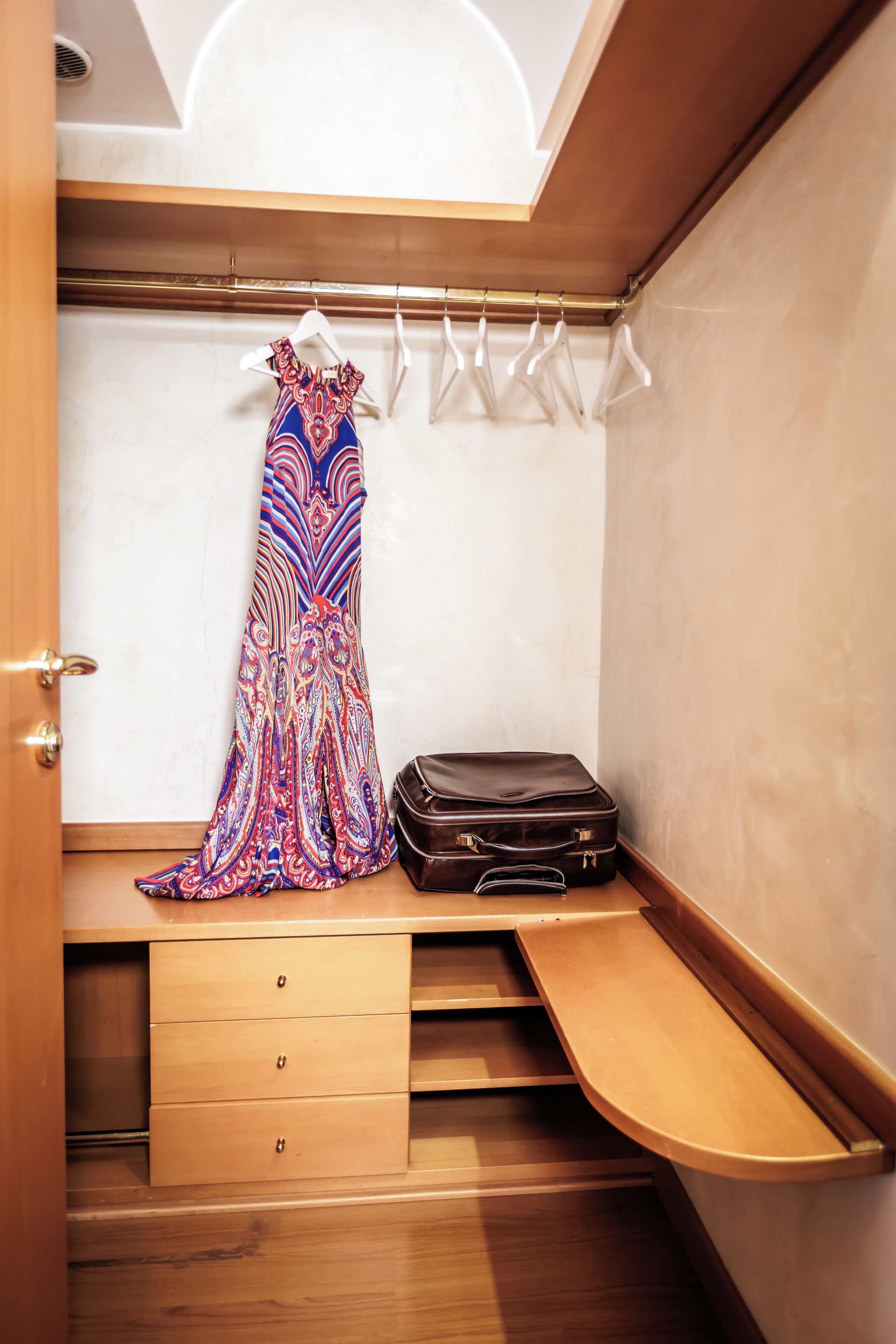 A walk-in closet with a hanging rack, a suitcase, and a wooden bench.