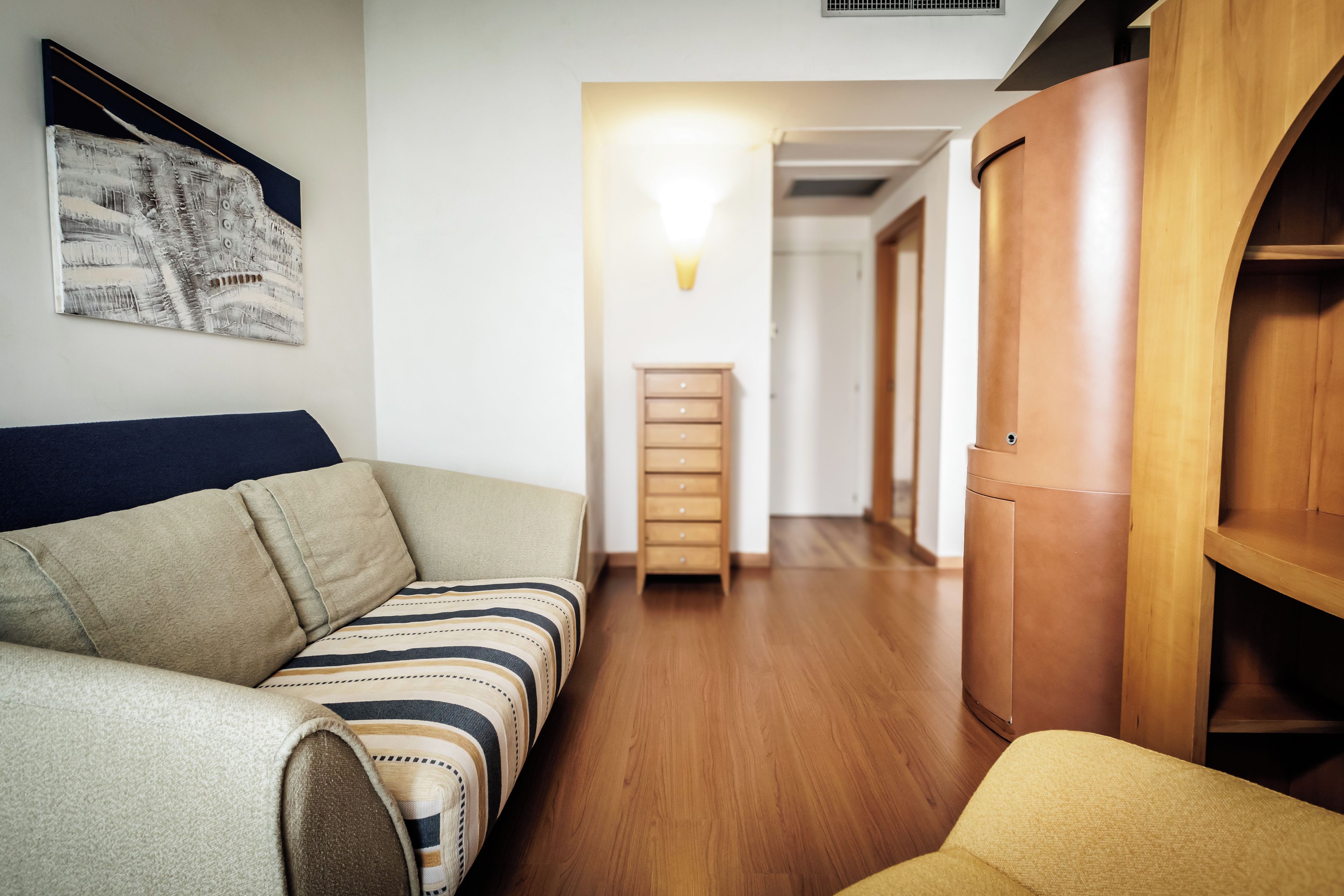 Una habitación con sofá, un armario de madera y un pasillo que conduce a otra estancia.