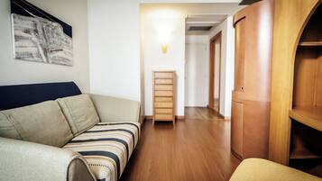 Una habitación con sofá, un armario de madera y un pasillo que conduce a otra estancia.