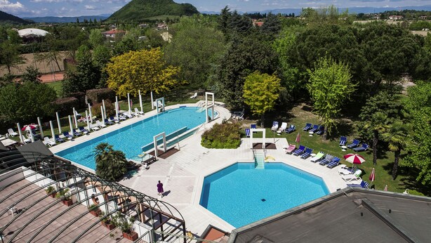 Ein Schwimmbecken mit mehreren Bahnen, Liegestühlen und einer kleinen Brücke.