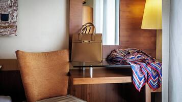 A hotel room with a brown leather chair, a wooden desk, a mirror, a lamp, and a colorful blanket.