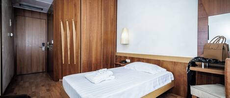 Habitación de hotel con cama, escritorio, silla, armario y lámpara de pared.