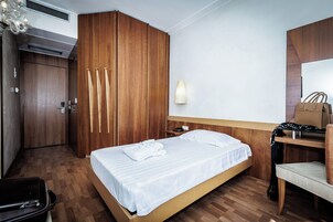 Habitación de hotel con cama, escritorio, silla, armario y lámpara de pared.