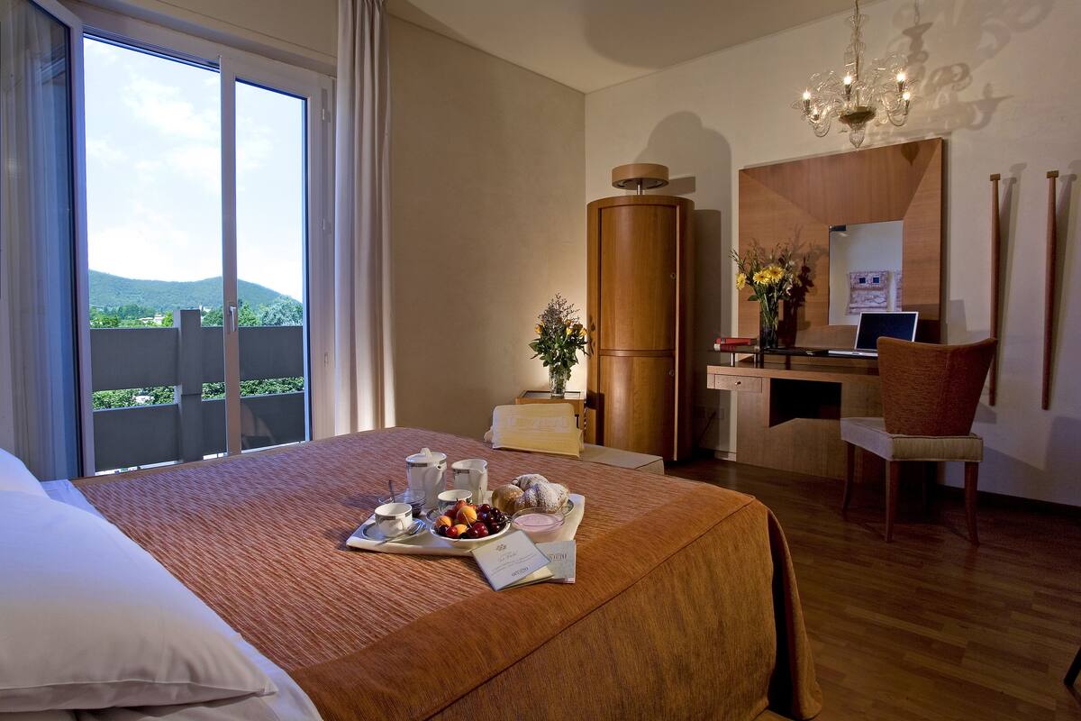 Une chambre d’hôtel avec un lit, un plateau de petit-déjeuner, un bureau et une vue sur la verdure.