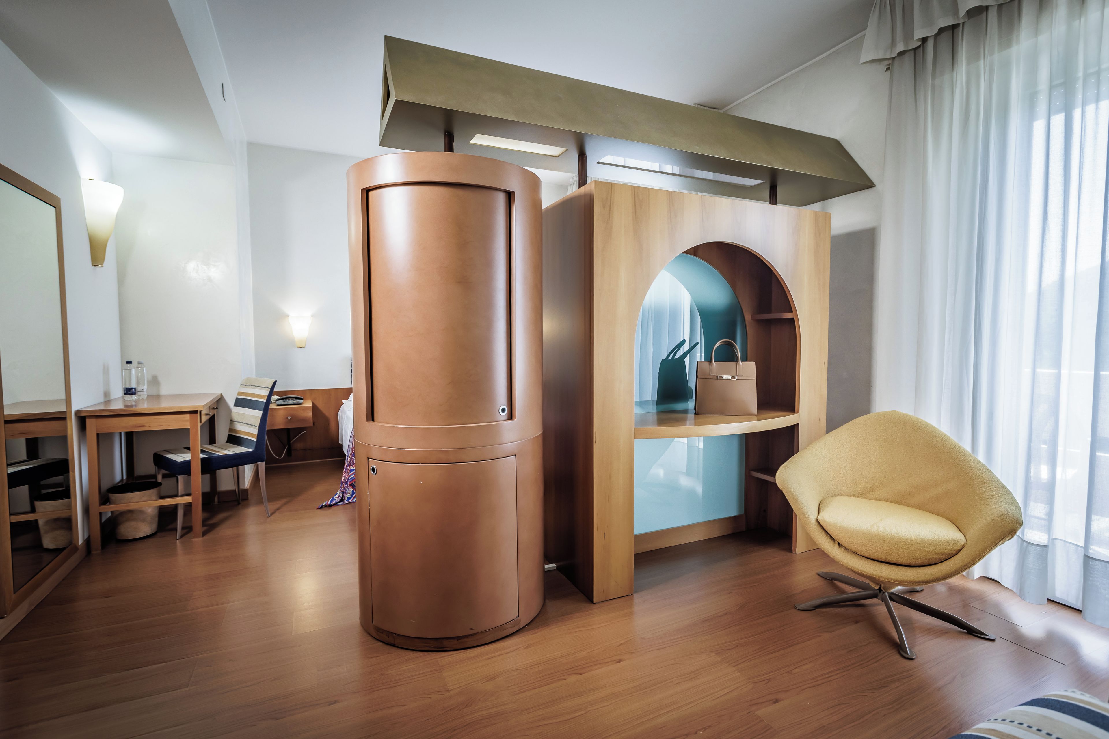 Una habitación de hotel moderna con un escritorio de madera, una silla, un armario y un espejo grande.