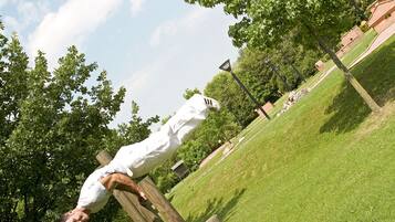 Two people performing pull-ups on wooden bars in a park with grass and trees.