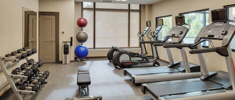 A gym with treadmills, dumbbells, a bench, and exercise balls.