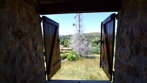 Ein Zimmer mit Stehwänden und einer offenen Holztür, das auf einen Baum und eine hügelige Landschaft blickt.