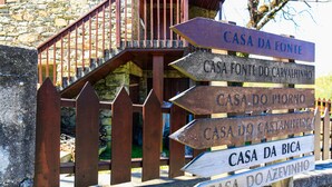 Ein hölzernes Wegweiser mit mehreren Richtungsschildern, die zu verschiedenen Orten wie Casa da Fonte, Casa do Piorno, Casa do Castanheiro, Casa da Bica und Casa do Azevinho weisen.