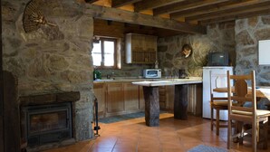 Eine rustikale Küche mit Steinwänden, Holzbalken, einem Kamin aus Stein und einem Holztisch mit Stühlen.