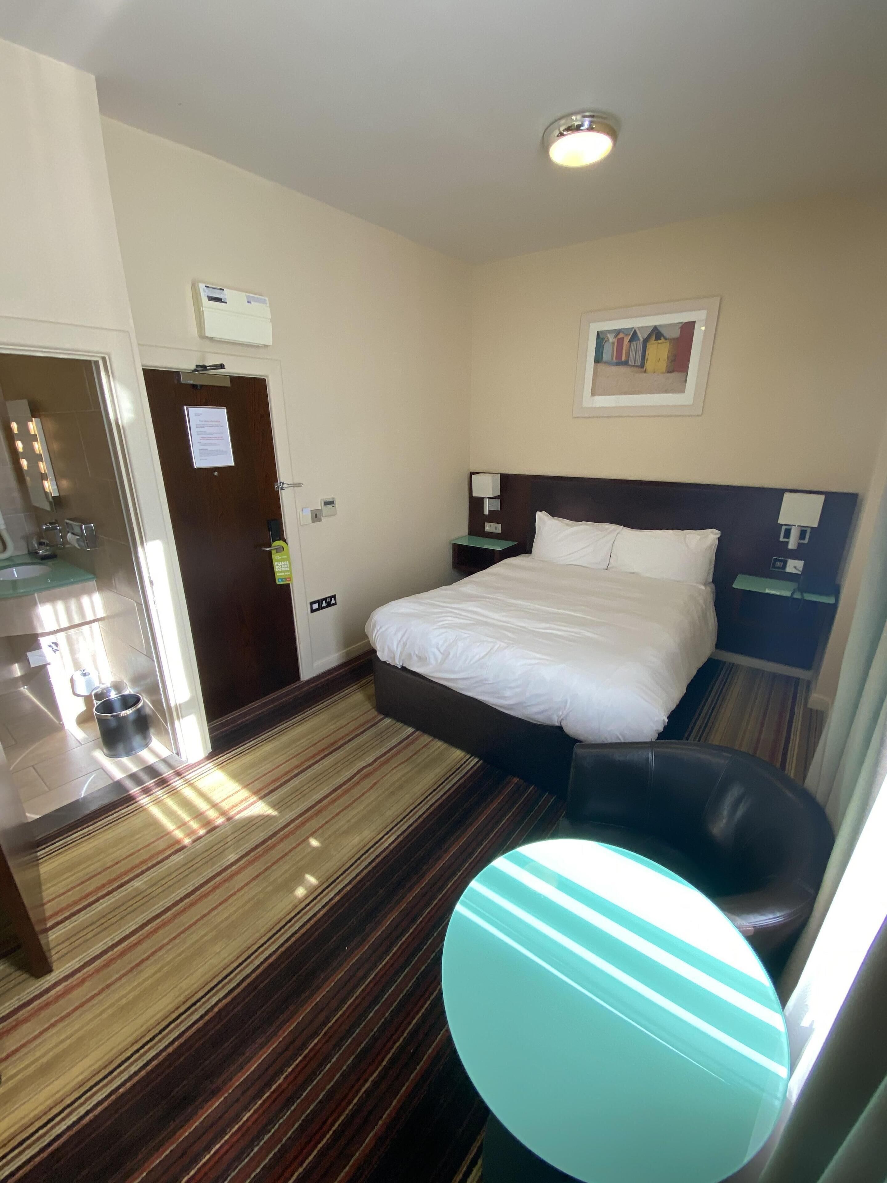A hotel room with a bed, a desk, a chair, and a small table.