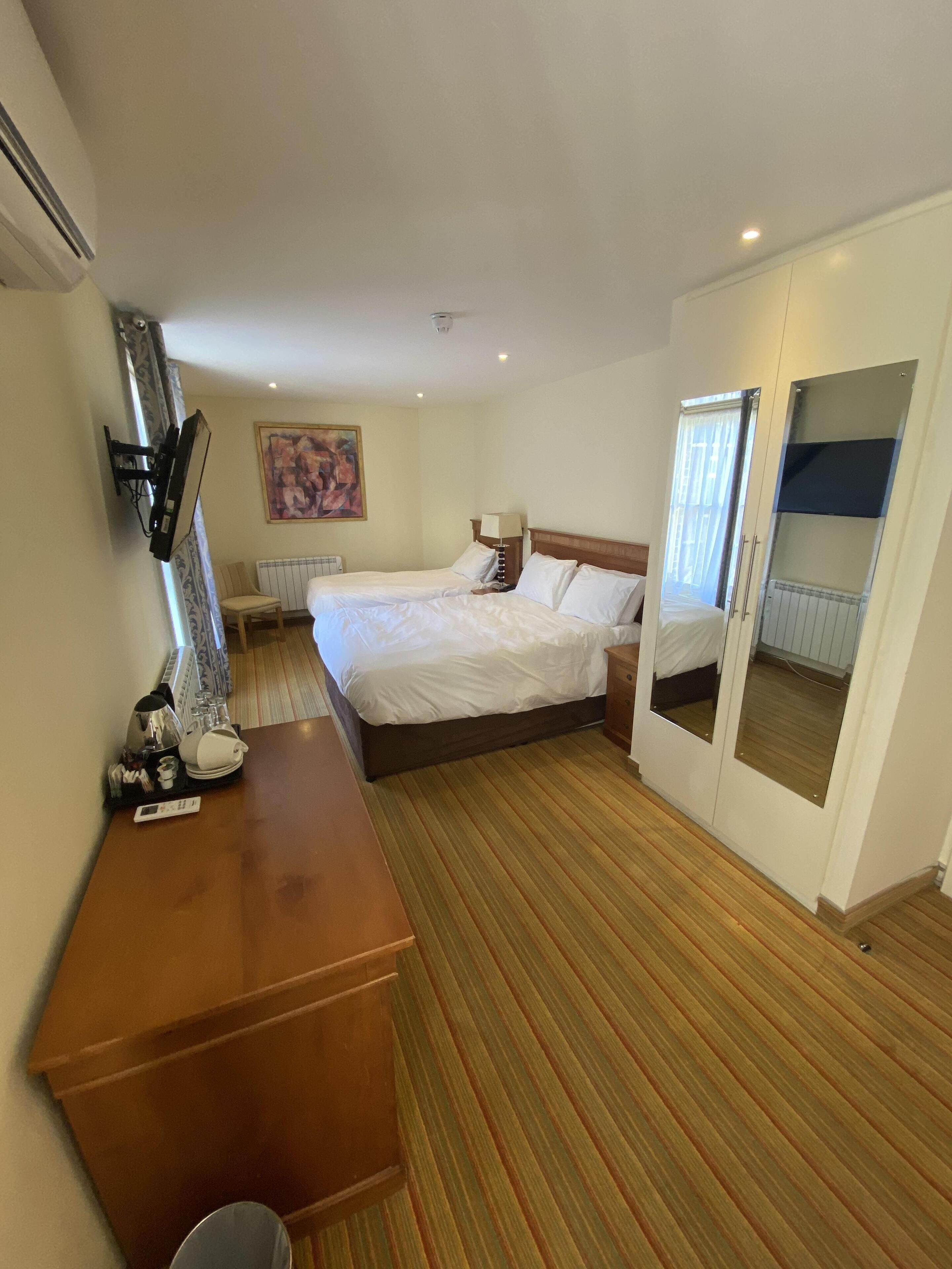 Een hotelkamer met een bed, nachtkastjes, een bureau met stoel, een schilderij aan de muur en een raam met gordijnen.