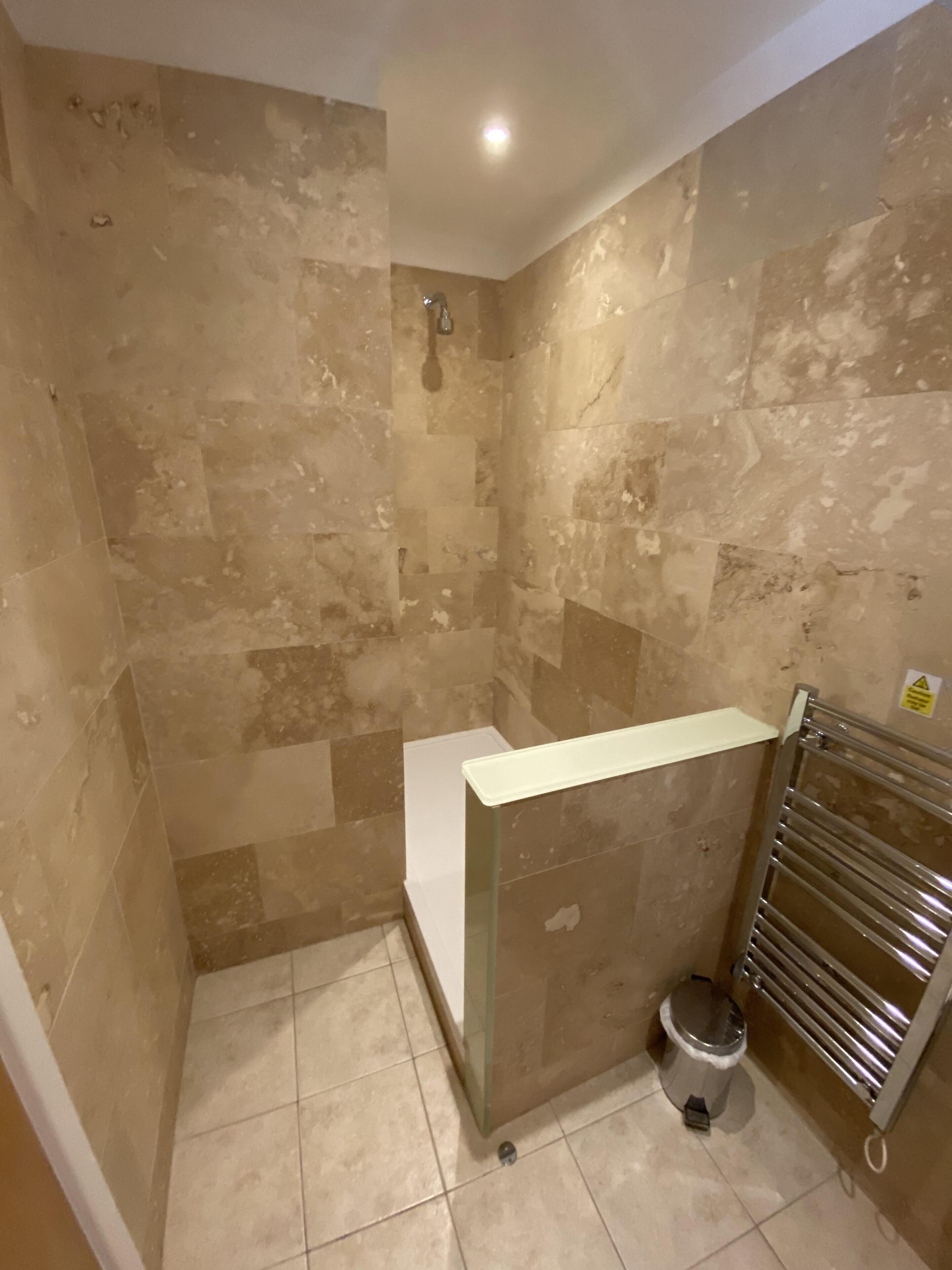 A small, tiled shower area with a glass partition and a metal towel rack.