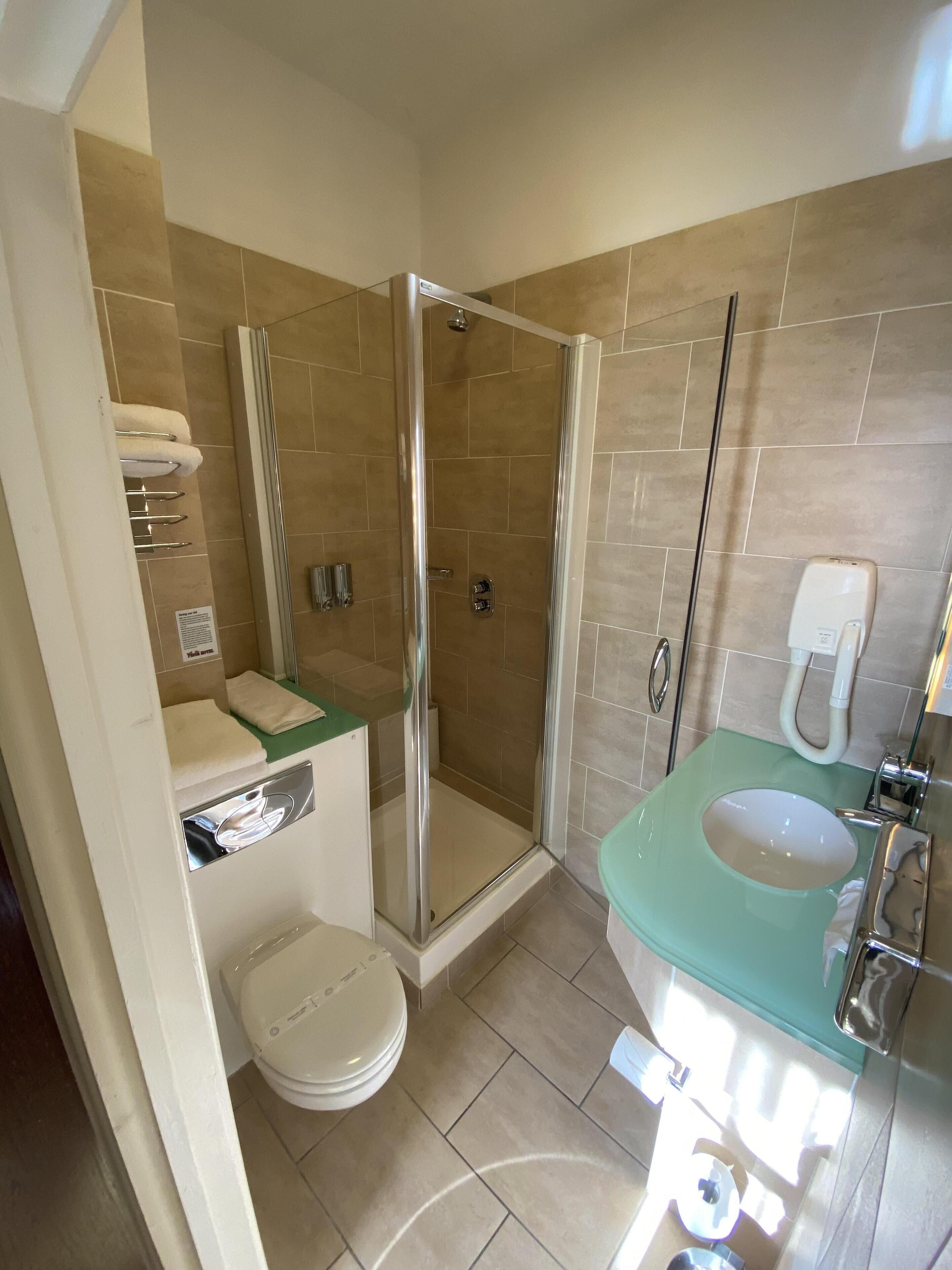 Et moderne badeværelse med et brusebad med glasvægge, et hvidt toilet, en grøn vask og et håndholdt brusehoved.