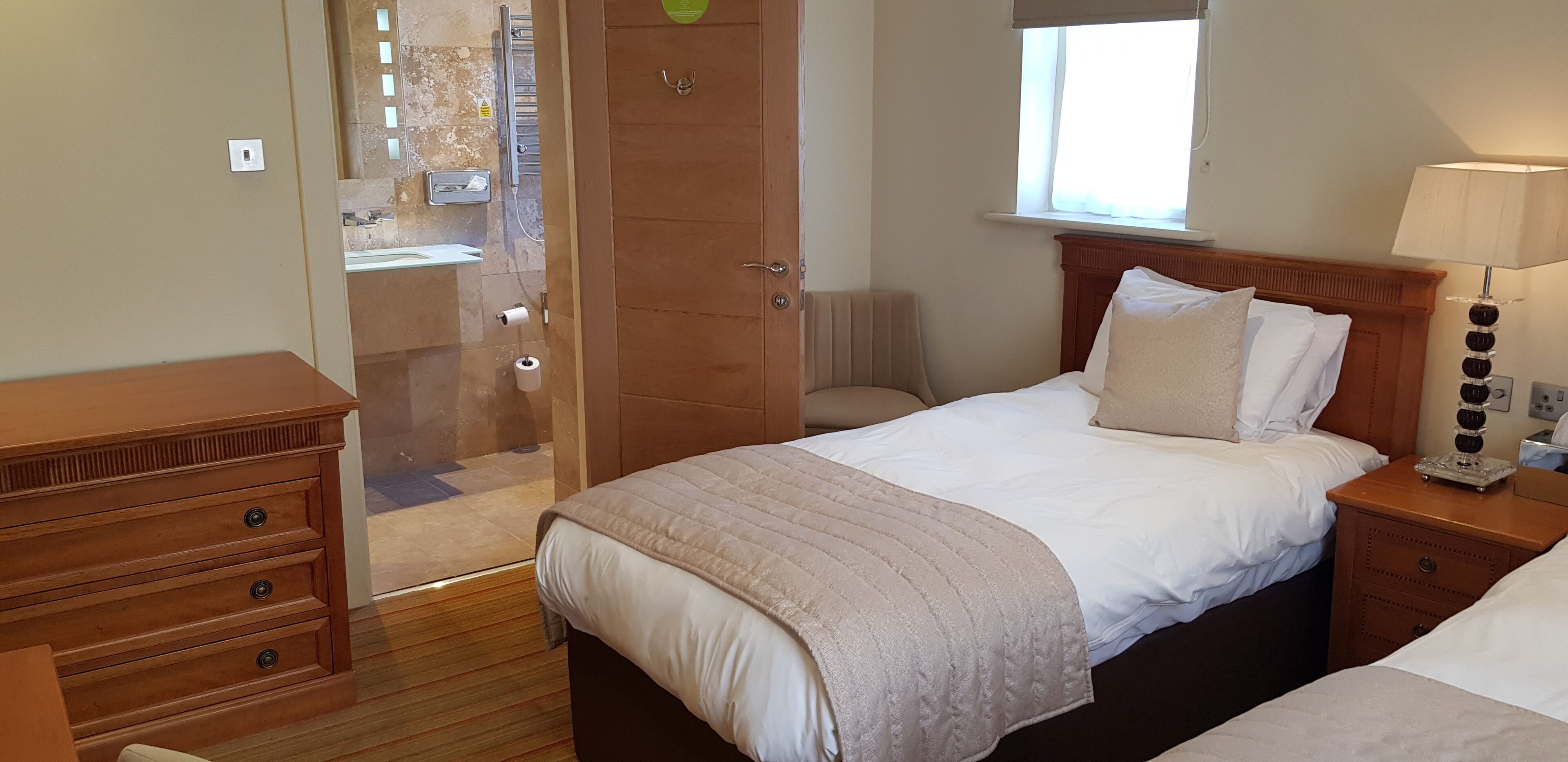 A bedroom with a bed, bedside table, lamp, and a wooden dresser.