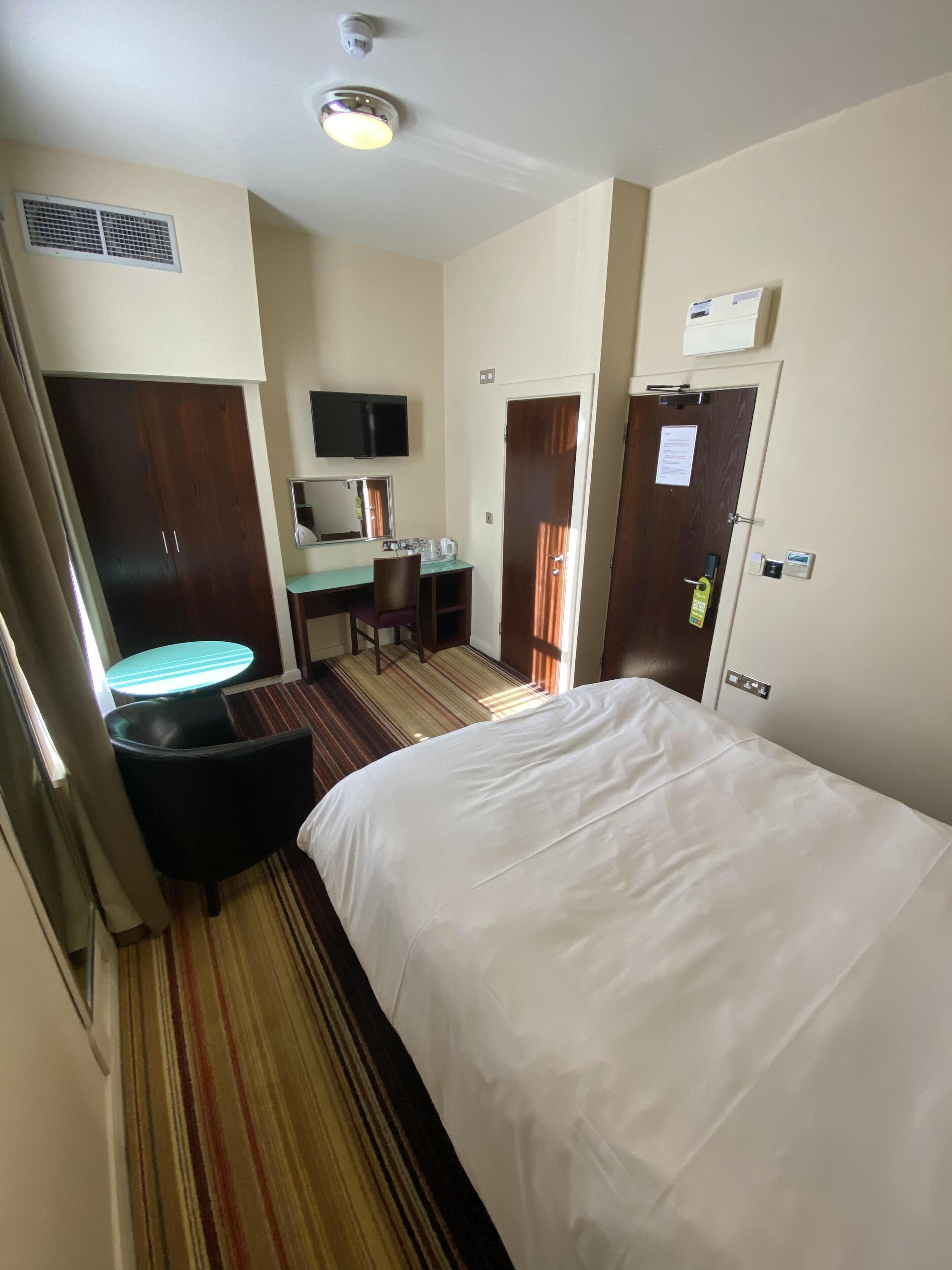 A hotel room with a bed, a desk, a chair, a television, and a minibar.