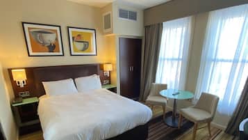 Hotelkamer met een groot bed, nachtkastje met lamp, een klein rond tafeltje met twee stoelen, en een kledingkast.