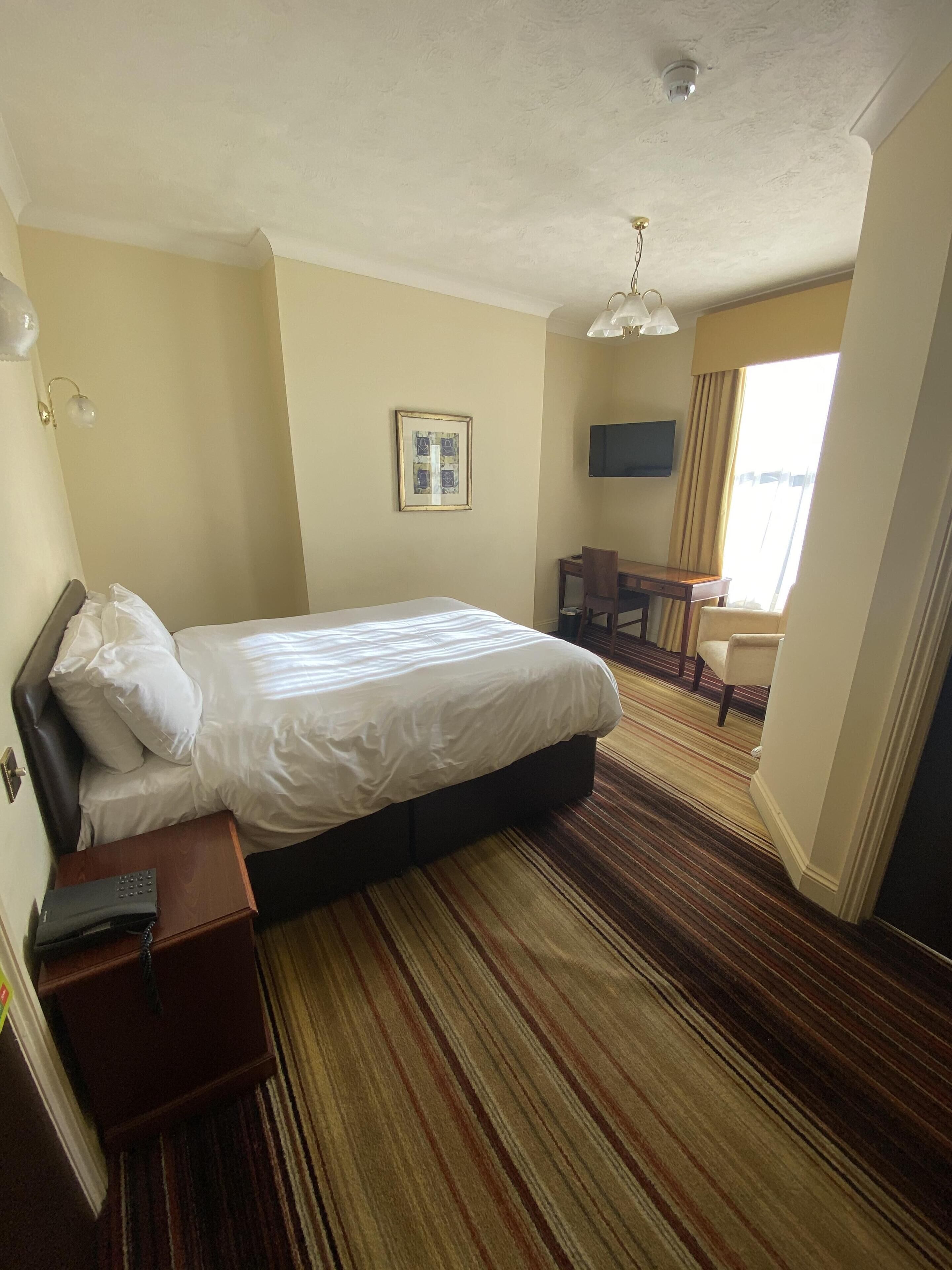 Habitación de hotel con una cama grande, un escritorio, una silla, un televisor y una ventana con cortinas.