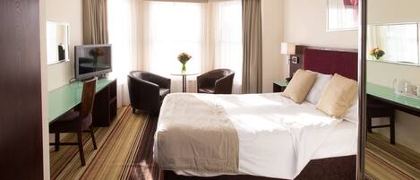 Habitación de hotel con una cama grande, un escritorio con computadora, una silla y una mesita con flores.
