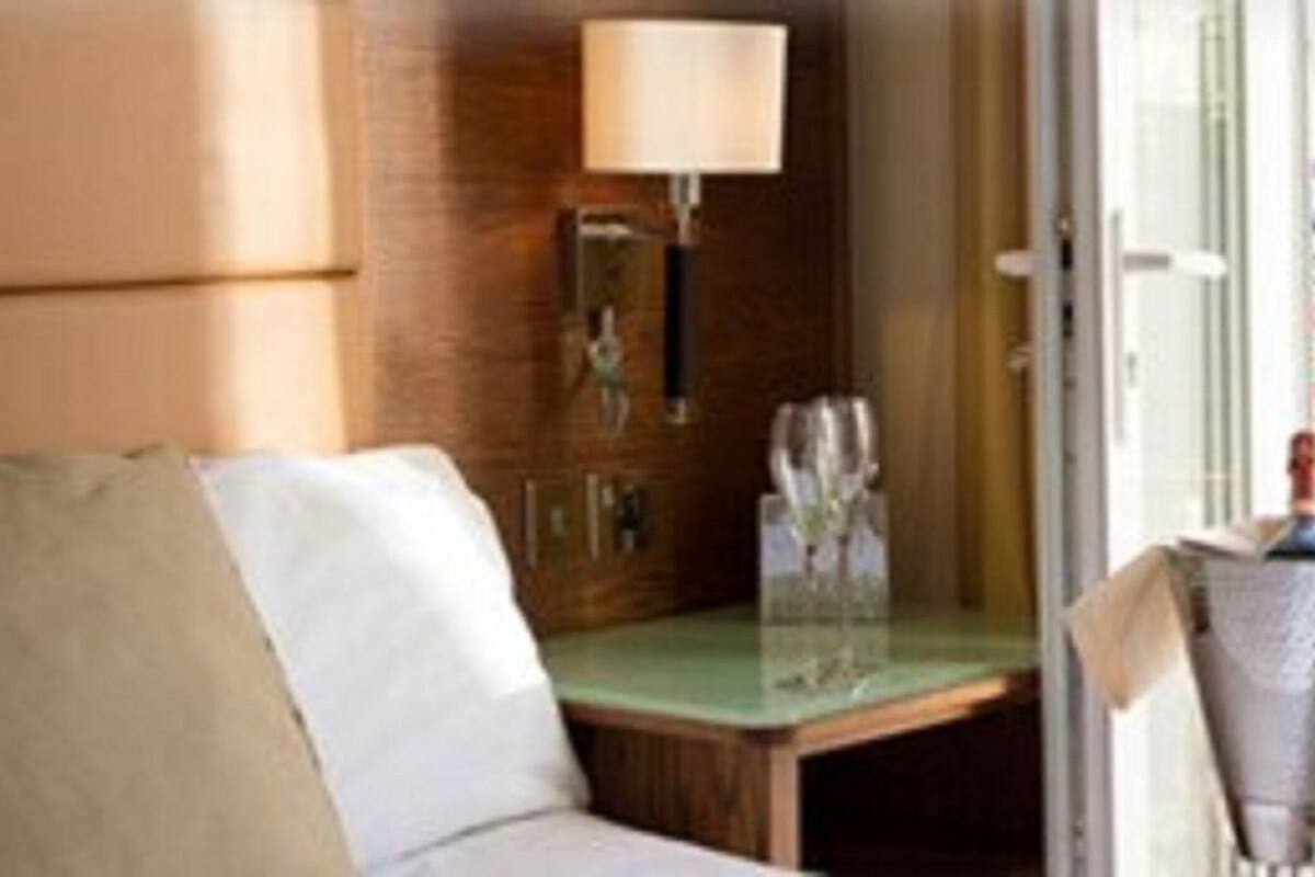 A hotel room with a sofa, a bedside table with a lamp, and a window.
