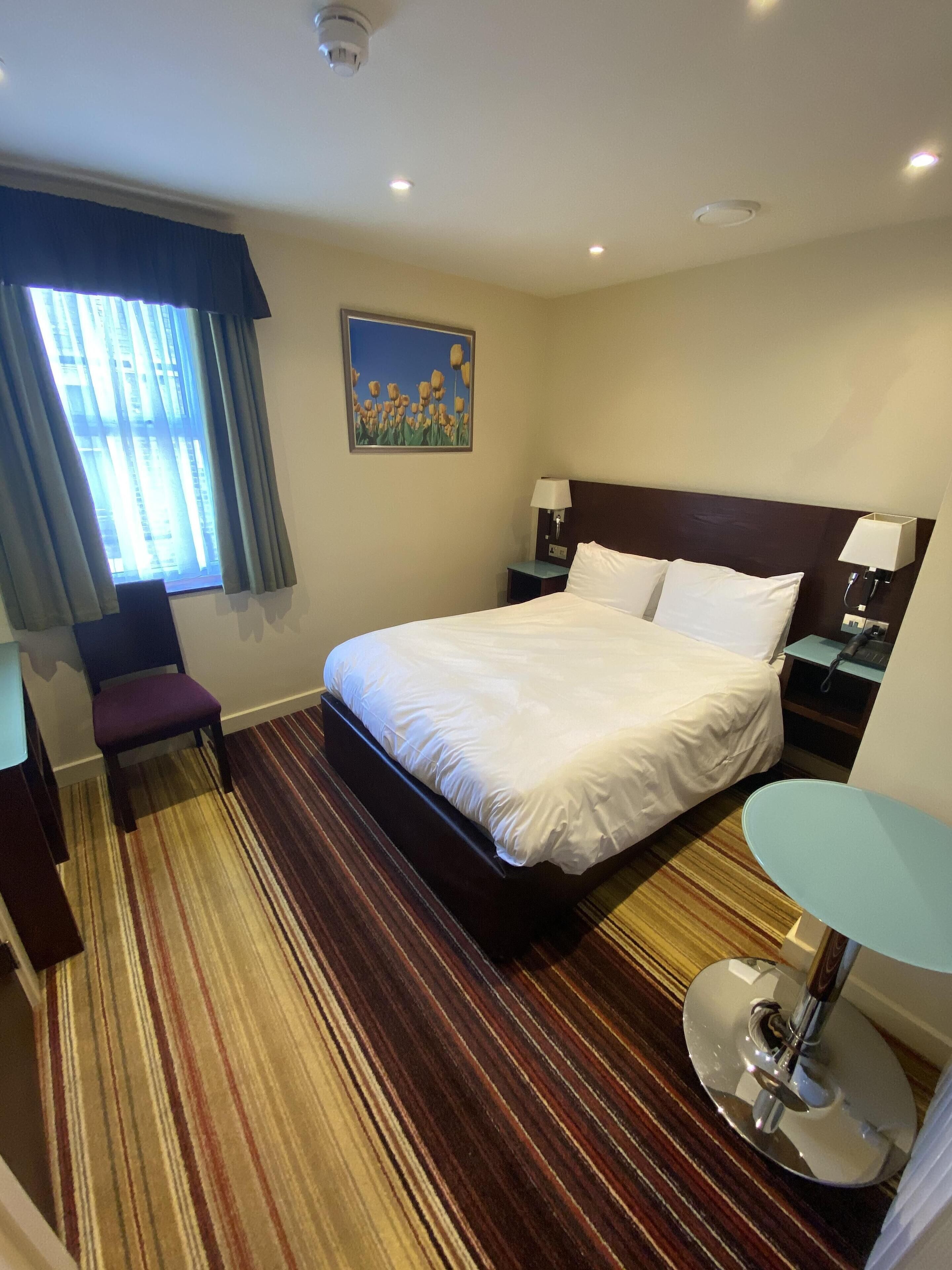Een hotelkamer met een groot bed, een bureau, een stoel, een klein tafeltje en een schilderij aan de muur.