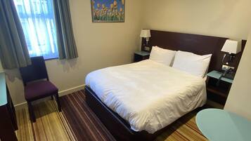 Habitación de hotel con una cama grande, un escritorio, una silla, una mesita y un cuadro en la pared.
