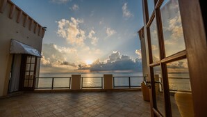 Een terras met uitzicht op zee tijdens de zonsondergang, met een betegelde vloer en een leuning.