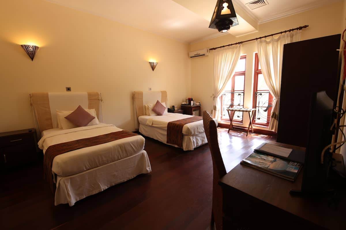 Une chambre d’hôtel avec deux lits, un bureau, une chaise, une télévision et une fenêtre avec des rideaux.