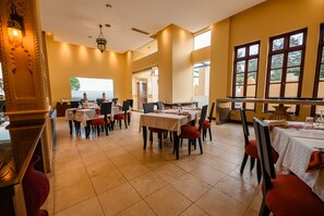 A spacious dining area with multiple tables and chairs, large windows, and a chandelier. - Cocoa Boutique Hotel (Mombasa)