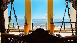 A balcony with a view of the ocean, ornate wooden furniture, and two potted plants.
