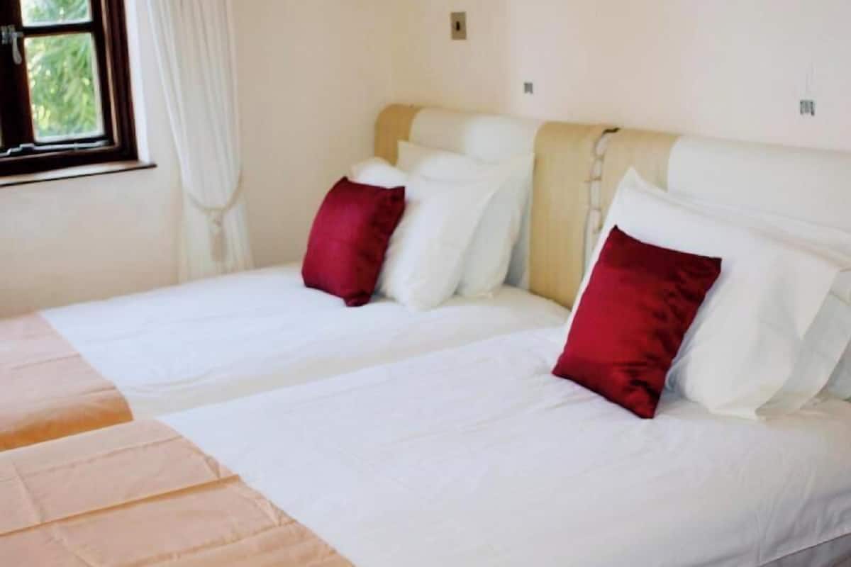 Un lit double avec des oreillers blancs et rouges, une tête de lit beige et une fenêtre avec des rideaux.