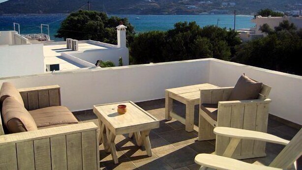 A rooftop terrace with outdoor furniture, a view of the sea, and a mountain in the background.