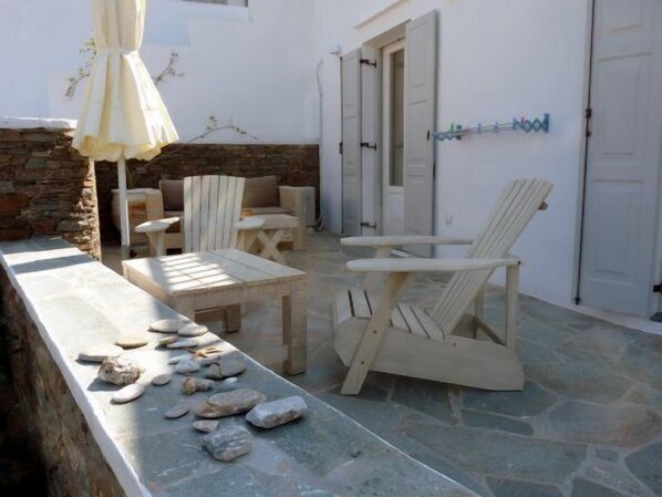 A stone-floored patio with wooden furniture, including a table and chairs, and a stone wall. - Aerina Luxury Apartments (Sifnos)