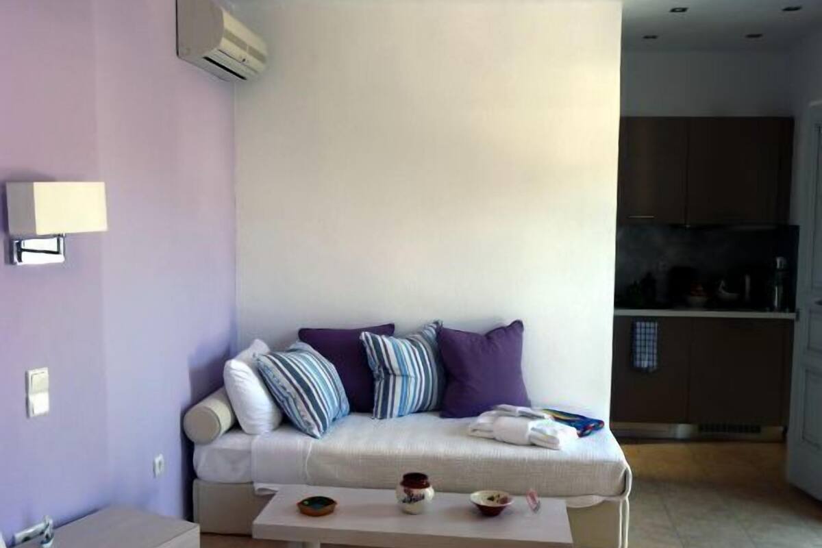 Un salon moderne avec un canapé, une petite table sur laquelle sont posés des bols, et un coin cuisine à l’arrière-plan.