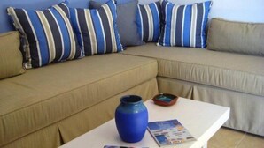 A beige sofa with striped pillows, a white table with a blue vase and magazines, and a small bowl.